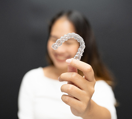 Closeup of patient holding a clear aligner while smiling