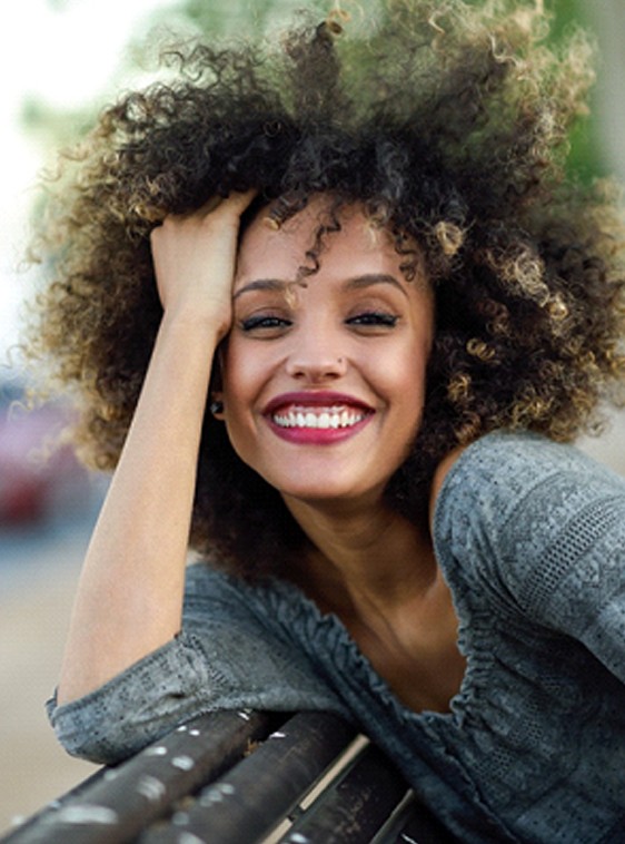 A young woman sitting on a park bench and smiling after learning she is eligible to undergo gum recontouring in Houston